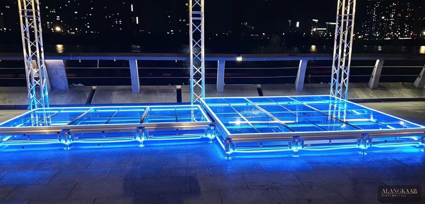 Glass LED stage glowing blue at night with truss towers