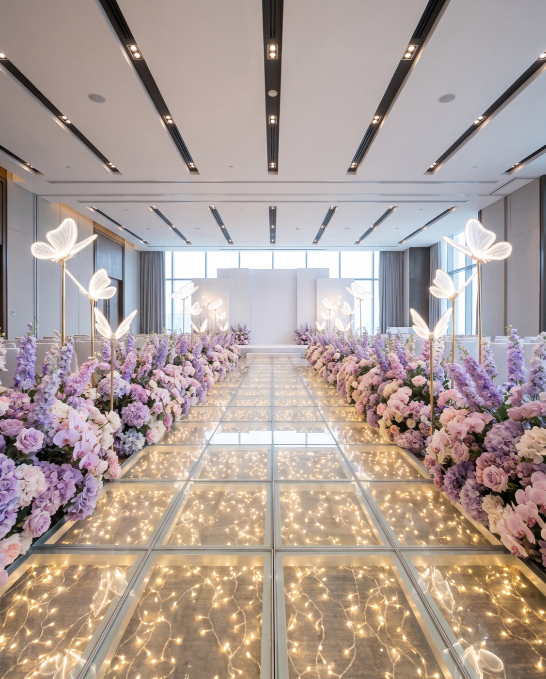 Lilac and pink flower hedges beside a glowing glass walkway with butterfly lamps