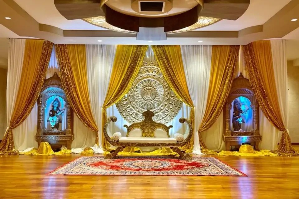 A real Alangkaar stage: gold and ivory drapes, a carved mandala backdrop, a gold bridal sofa and a red carpet