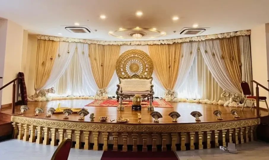 A raised stage with gold and white drapes, a white floral border and a round gold backdrop behind an ivory sofa