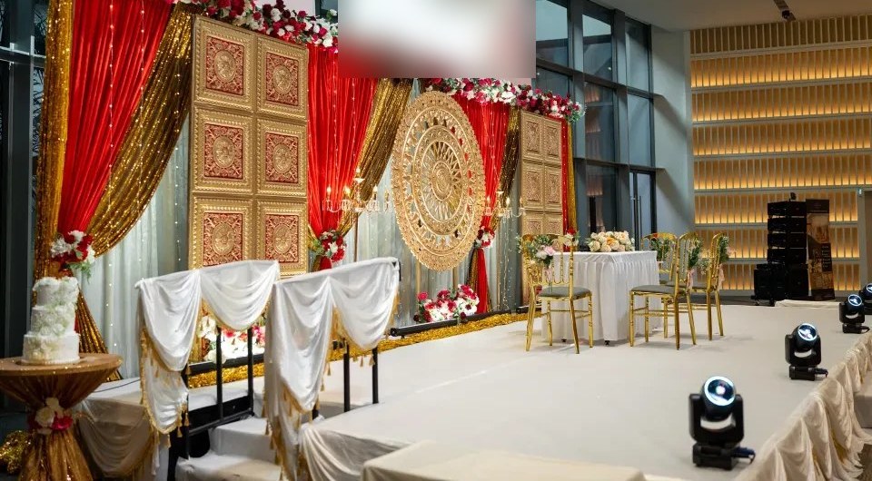 A stage with red and gold drapes, carved gold panels, a round gold backdrop and flowers on a white floor