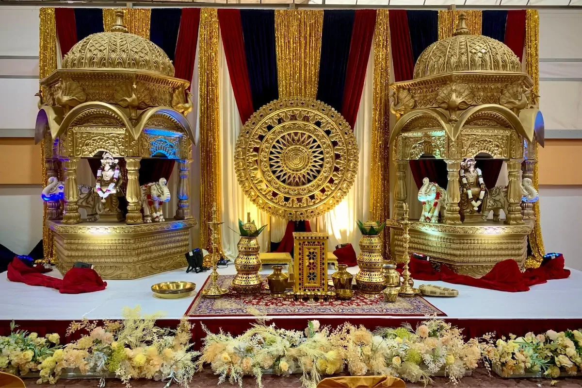 A gold temple-style mandap stage with twin domed shrines, styled by Alangkaar
