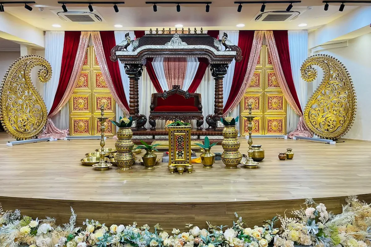 A carved wooden mandap with gold paisley panels and brass kalasams, styled by Alangkaar